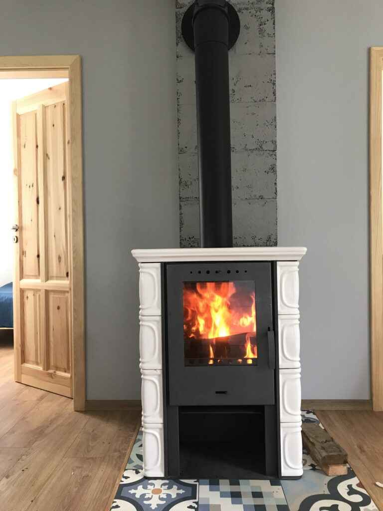 wolnostojący kominek kaflowy w białym kolorze ustawiony w pokoju